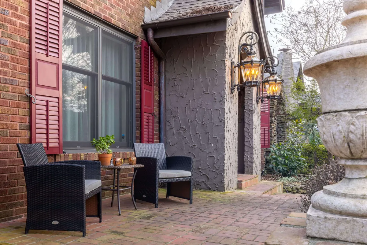 An outdoor seating area with wicker chairs, a small table, decorative lanterns, and a brick wall backdrop. The setting is intimate and ideal for socializing, enjoying morning coffee, or winding down in the evening.