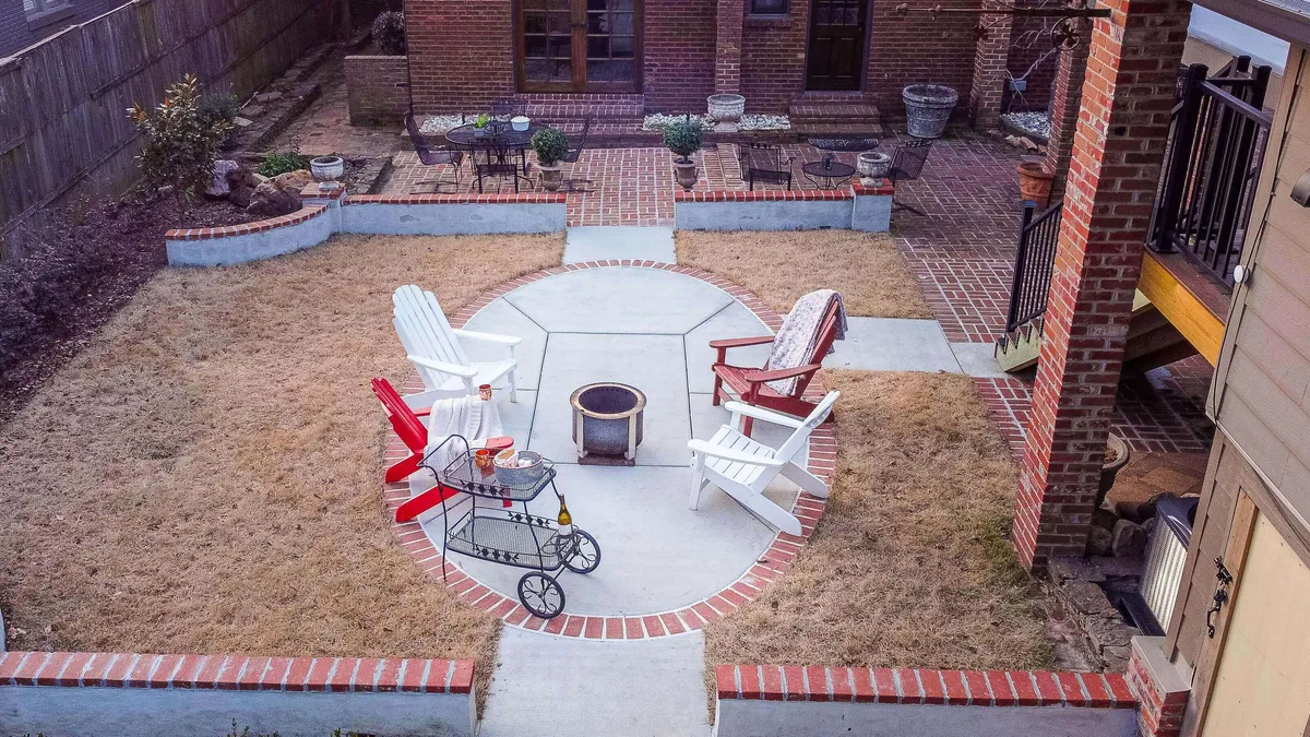 A charming backyard scene featuring a fire pit surrounded by Adirondack chairs, brick pathways, and lush gardens. The setting is cozy and designed for communal gatherings, with ample outdoor seating for friends to relax and connect.