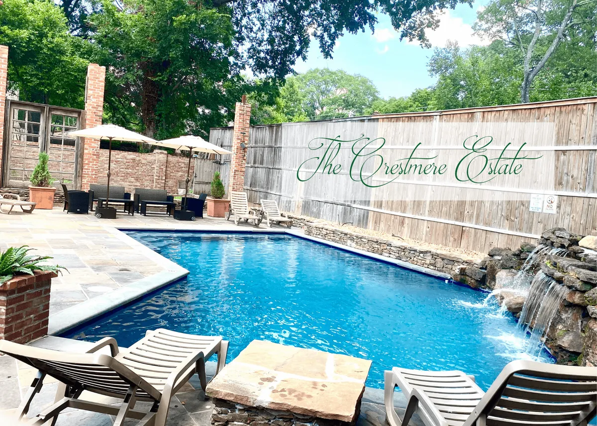 A luxurious saltwater swimming pool is the focal point, framed by lush landscaping and soft evening light. The pool area features a tranquil waterfall and inviting outdoor seating, while the Crestmere Estate sign gives a sense of exclusivity and privacy. The overall setting is serene and upscale, perfect for swimming, lounging, or gathering with friends and family.