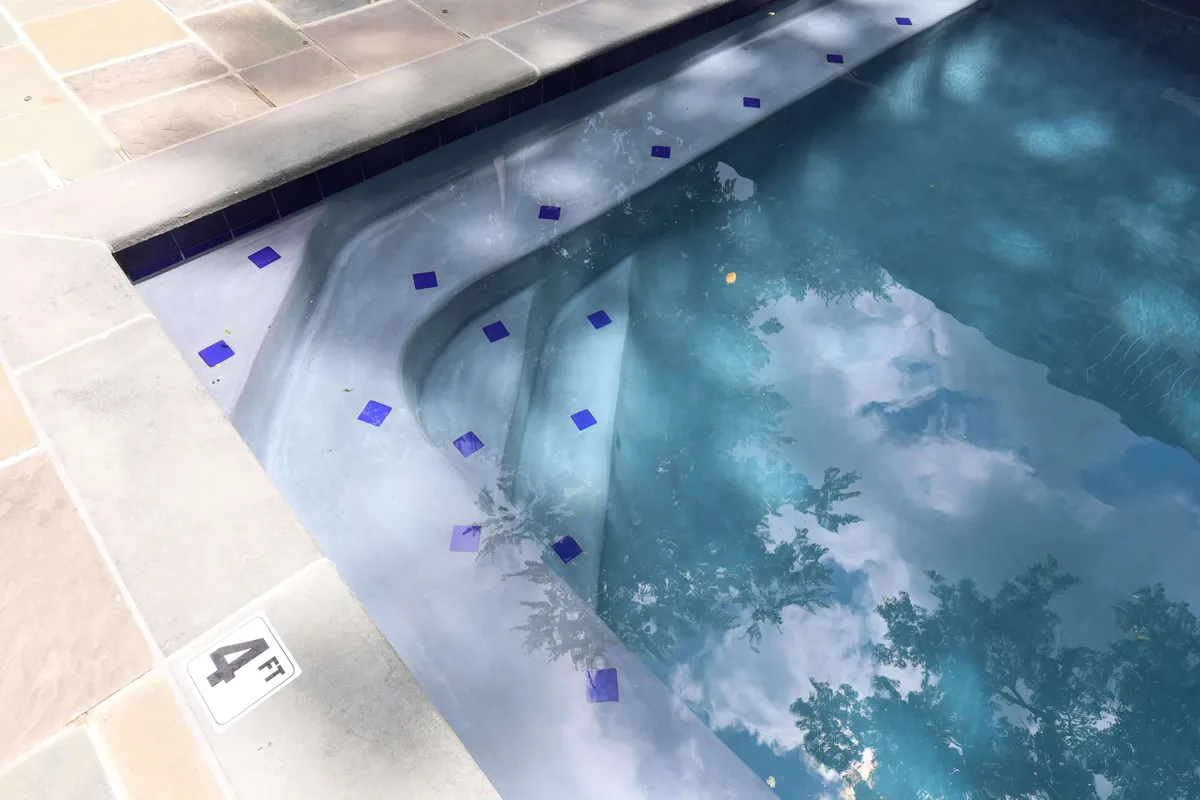 A tranquil view of the estate’s pool area, with sparkling blue water, elegant blue tiles, and a surrounding deck. The serene setting is nestled within the garden, suggesting relaxation after a day of exploring.