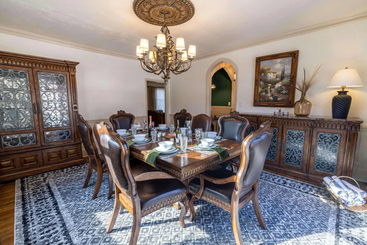 A formal dining room with a large dining table, a sparkling chandelier, a sideboard, and classic wall art. The space is arranged for gatherings, with elegant lighting and tasteful decor that evoke both sophistication and warmth.